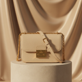 Sac bandoulière messager crème avec quincaillerie dorée et longue bandoulière réglable, posé sur un socle de pierre claire
